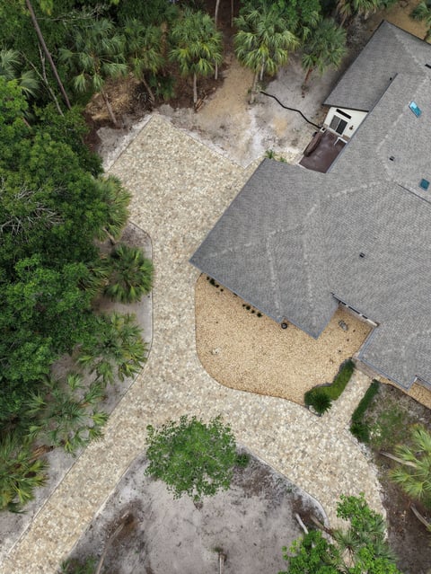 Aerial view of a house roof with gravel pathway, surrounded by dense green trees and vegetation