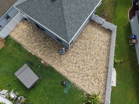 Aerial view of a residential backyard with a paver patio, green lawn, small shed, and house roof